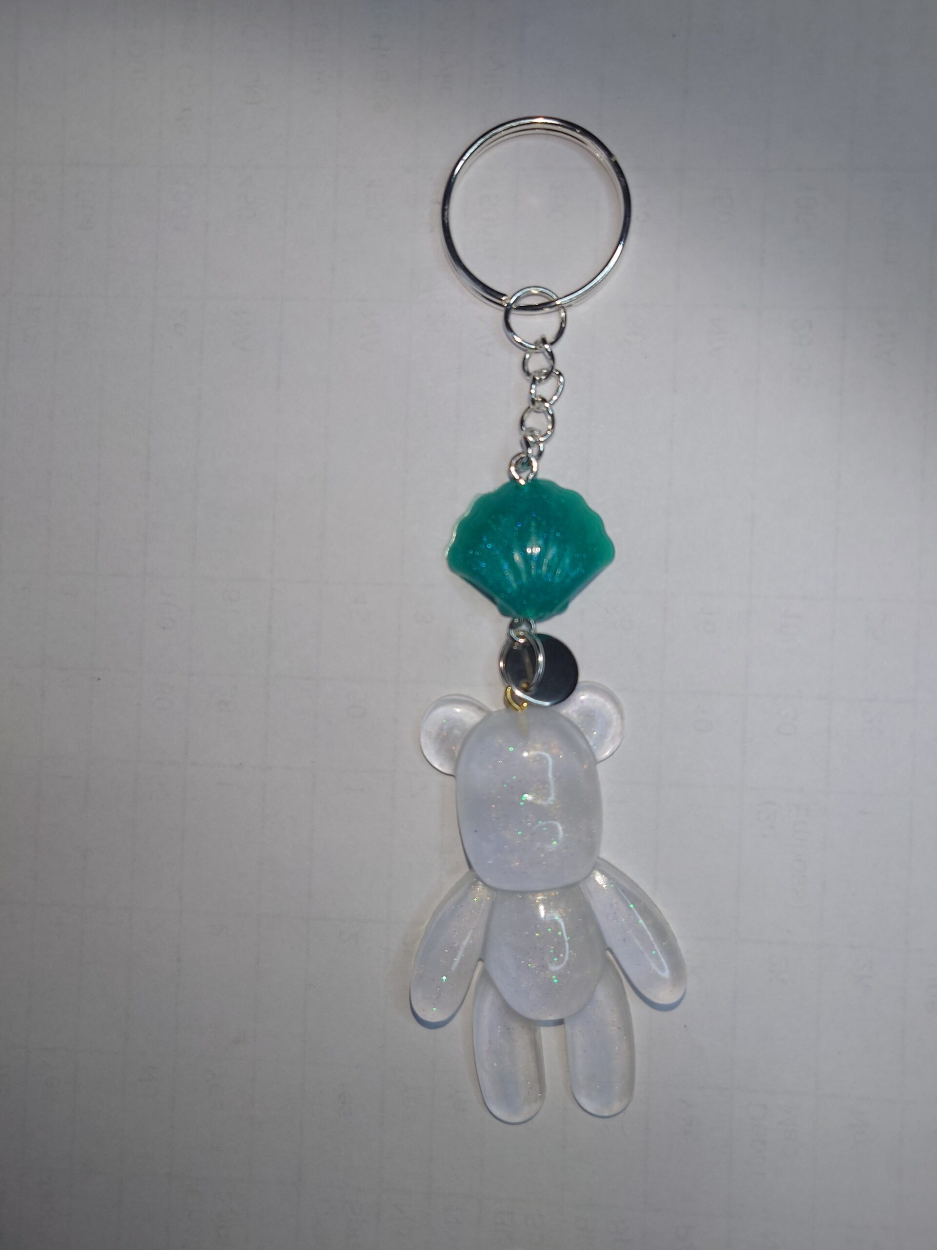 This is a keychain, of a standing TeddyBear character, in an opaque clear resin with hints sparkles and a green shell decoration, attached on a keychain.